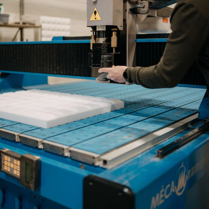 Des mains travaillent sur une machine qui découpe de la mousse de mélamine