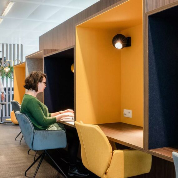 Une dame est assise sur un fauteuil bleu et travaille sur son ordinateur