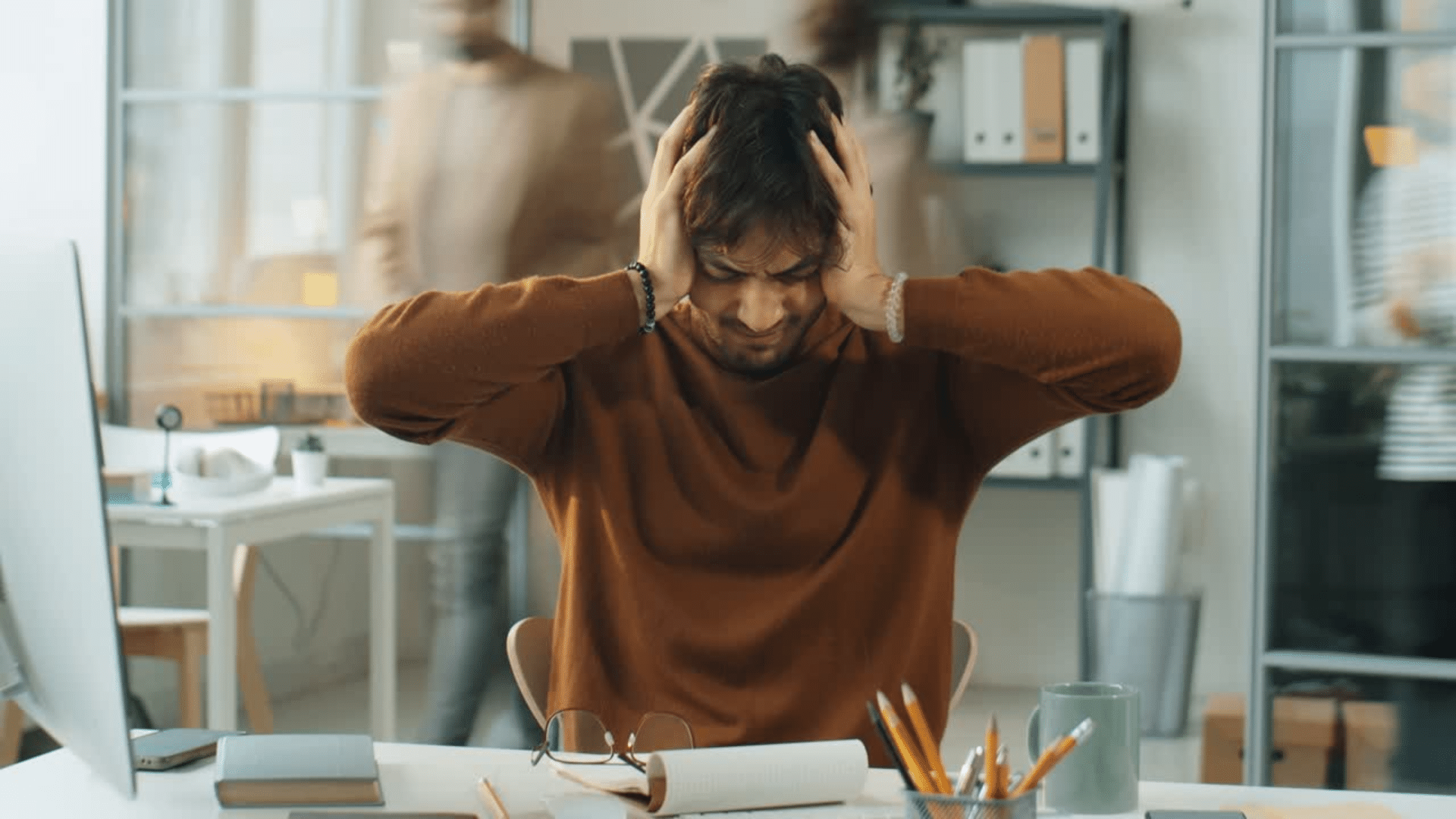 Un homme dans un bureau se tient la tête à cause du bruit